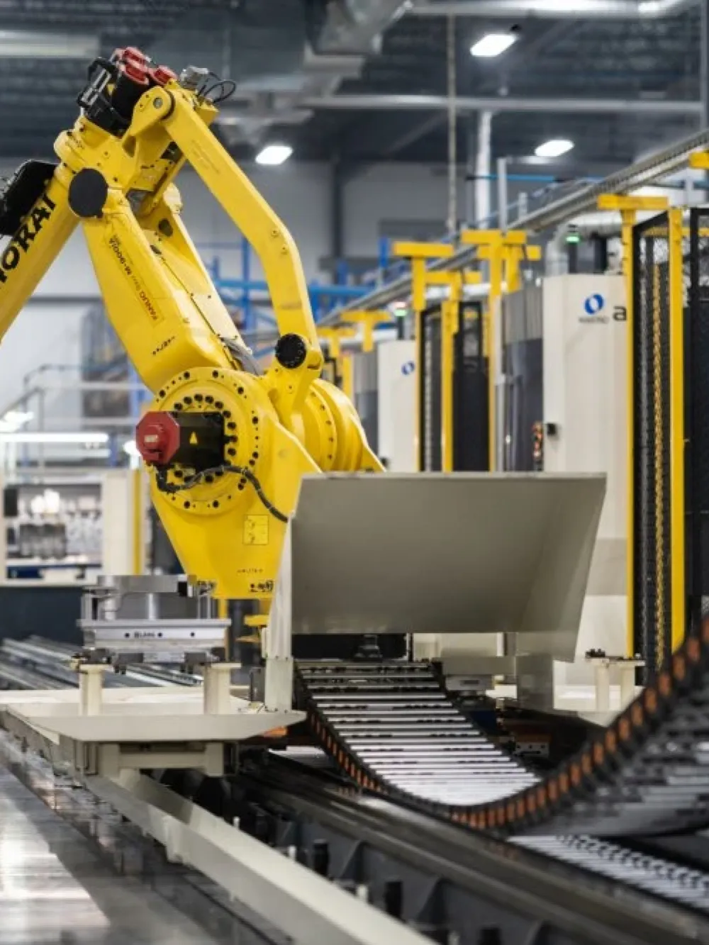 Bras robotisé jaune opérant dans une ligne de production automatisée, manipulant des pièces métalliques dans un environnement industriel. 