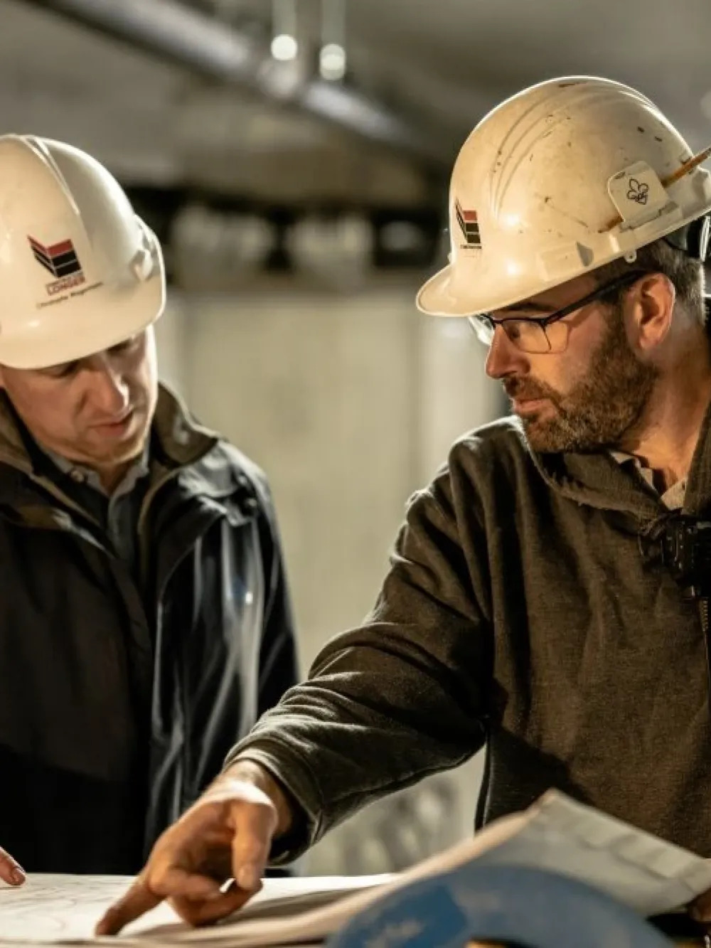 Deux personnes portant des casques de sécurité consultent des plans et discutent sur un chantier de construction.