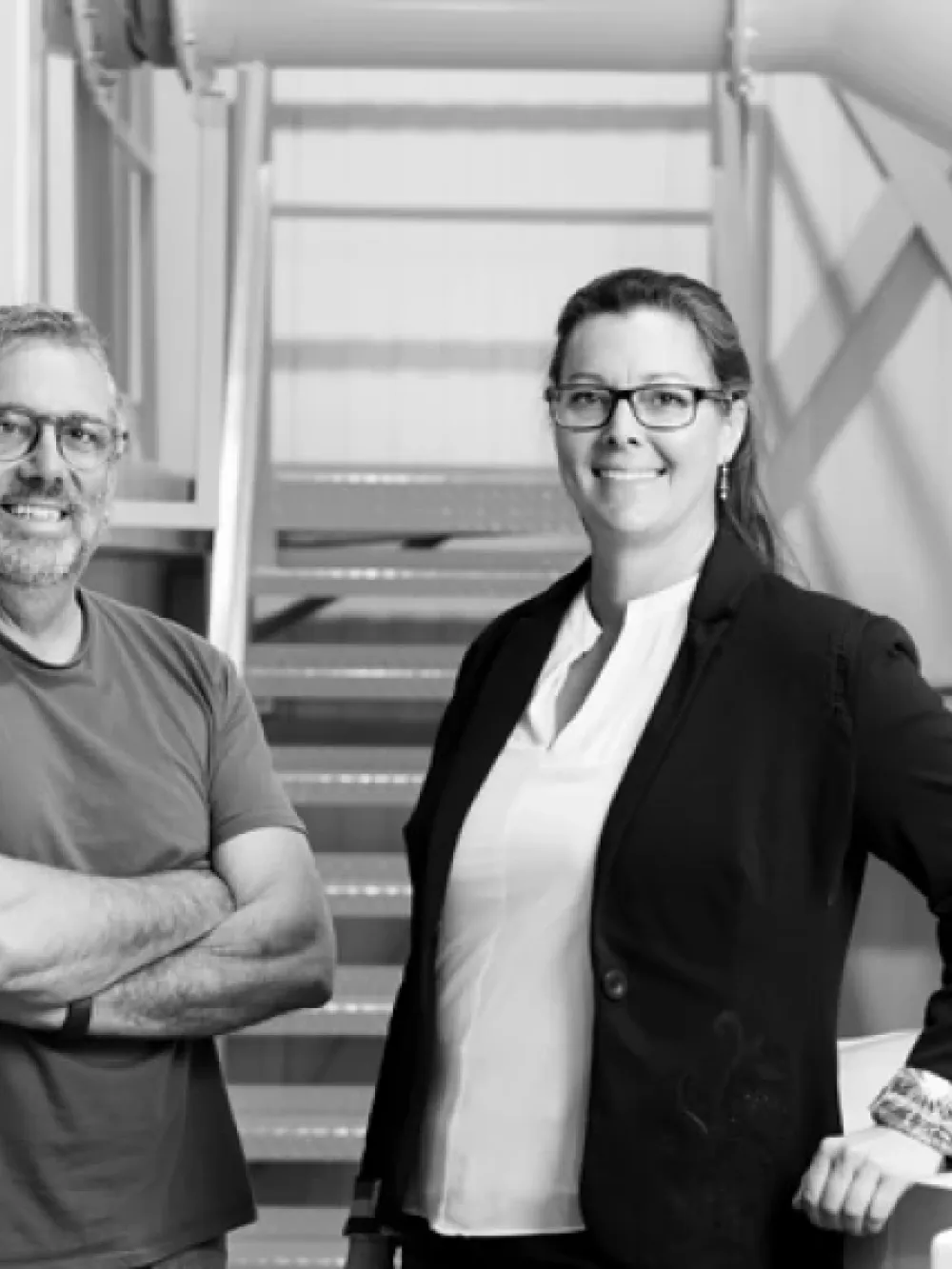 Deux personnes posent dans un environnement industriel, devant un escalier métallique et de larges conduits. 