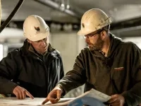 Deux personnes portant des casques de sécurité consultent des plans et discutent sur un chantier de construction.