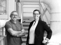 Deux personnes posent dans un environnement industriel, devant un escalier métallique et de larges conduits. 